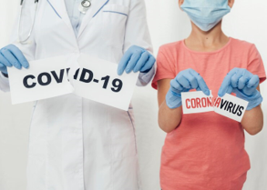The image shows a healthcare professional and a young person, both wearing gloves and masks, tearing apart signs labeled "COVID-19" and "CORONAVIRUS," symbolizing the fight against the pandemic and the hope of overcoming the virus. Designed by freepik